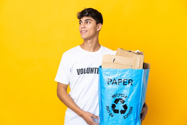Man holding a recycling bag full of paper to recycle over yellow thinking an idea while looking up