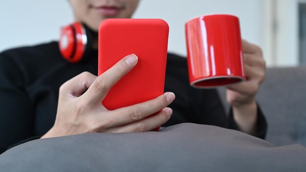 Man holding red cup of coffee and using smart phone