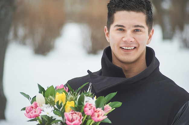 Man holding red gift box with beautiful bouquet of blooming pink, yellow and white tulips and white chrysanthemums with green leaves, outdoors