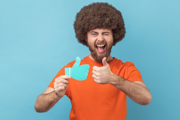 Man holding and showing like or thumbs up paper shape sign looking at camera with toothy smile