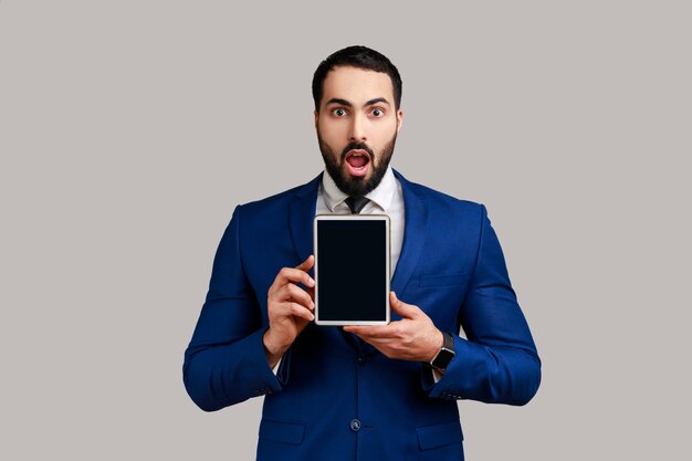 Man holding and showing tablet with blank screen with shocked face copy space for advertisement