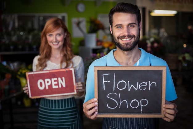 Мужчина держит планшет со знаком цветочного магазина и женщина держит открытую вывеску