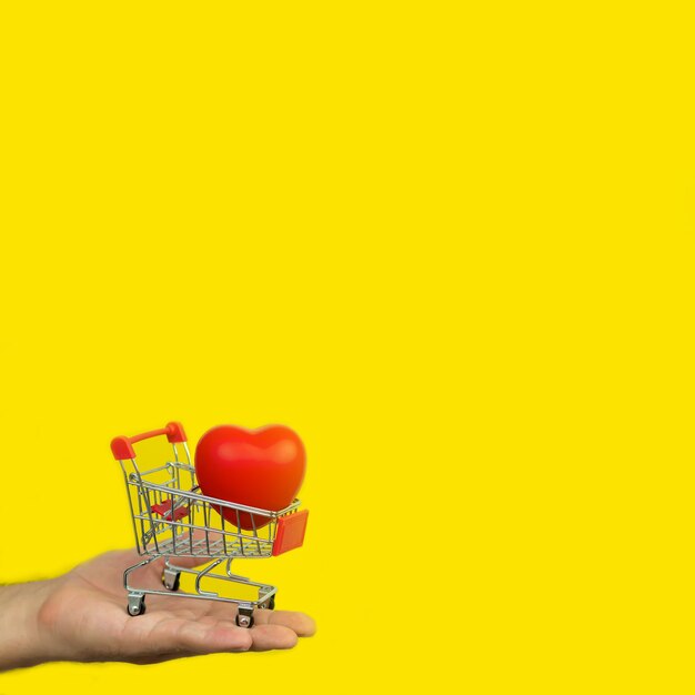 Man holding small cart with red heart on yellow background