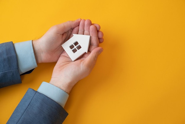 Man holding a small wooden house in the hand isolated of yellow background