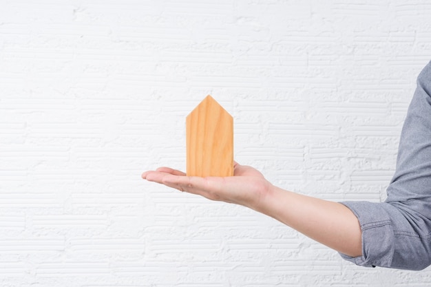 A man holding a small wooden house on his hand with white wall.