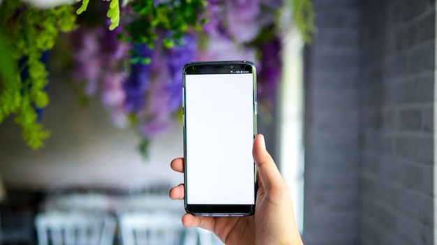 Photo man holding smartphone display white screen for mockup app on blur background in decoratio