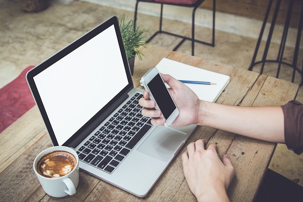 man holding smartphone on table with laptop and coffee