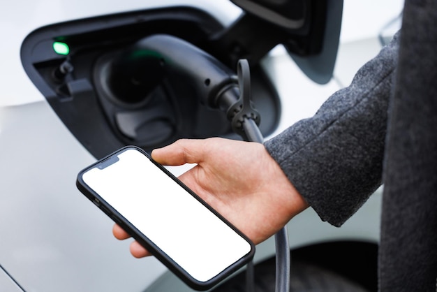 Photo man holding smartphone while charging car at electric vehicle charging station closeup ev charging