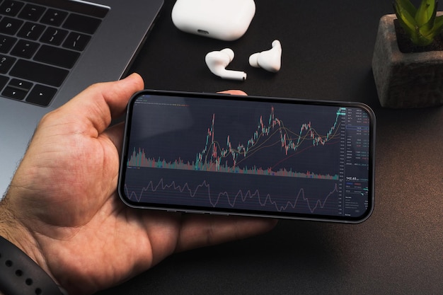 Man holding a smartphone with financial stock market graph on the screen on black background table Office environment Stock Exchange