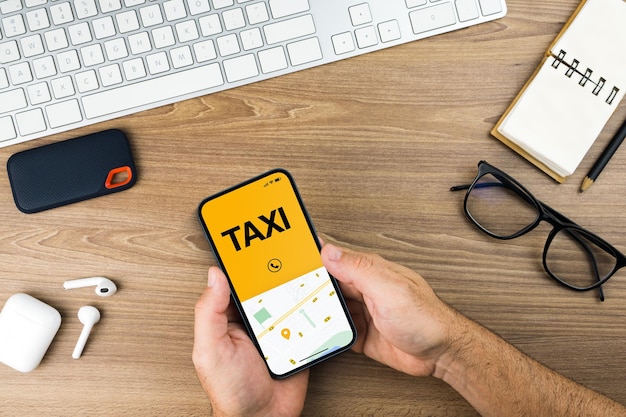 Man holding a smartphone with Taxi Service app on the wooden table. Office environment. Mobility service provider worldwide.