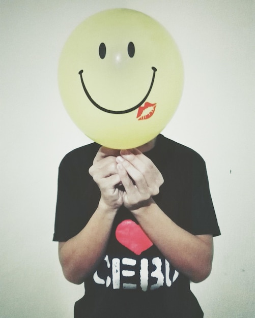 Man holding smiley face balloon against white background