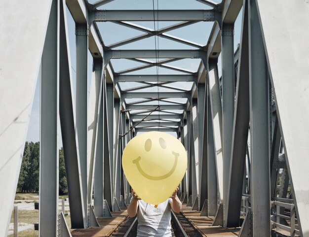 Foto uomo con un palloncino con la faccia sorridente sul ponte ferroviario