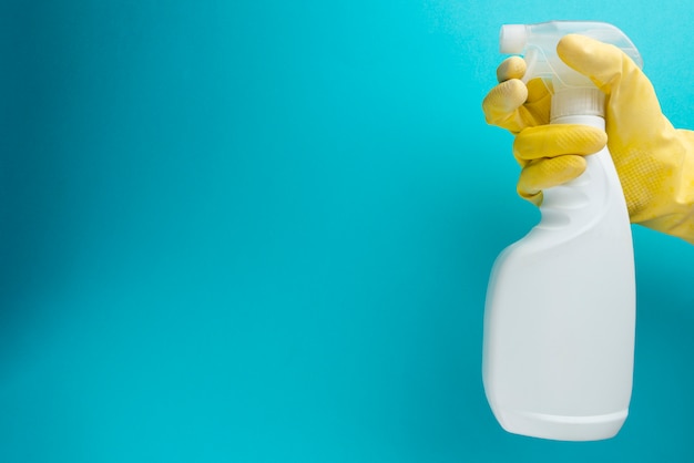 Man holding spray bottle of cleaning product on blue wall.