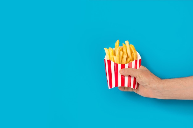 Man holding a striped box with fried potatoes on a blue background