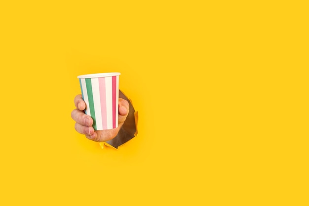 Man holding a striped party glass through a hole in yellow