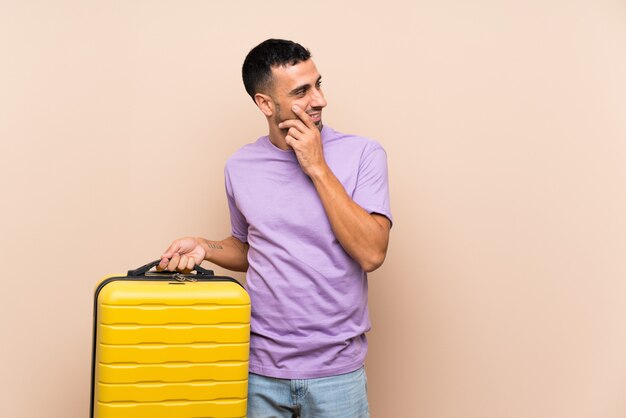 Man holding a suitcase over isolated wall thinking an idea and looking side