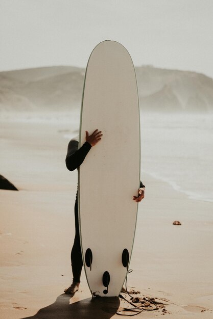 Man holding surfboard while standing on shore at beach