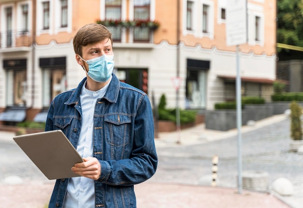 Man holding a tablet while wearing a medical mask with copy space