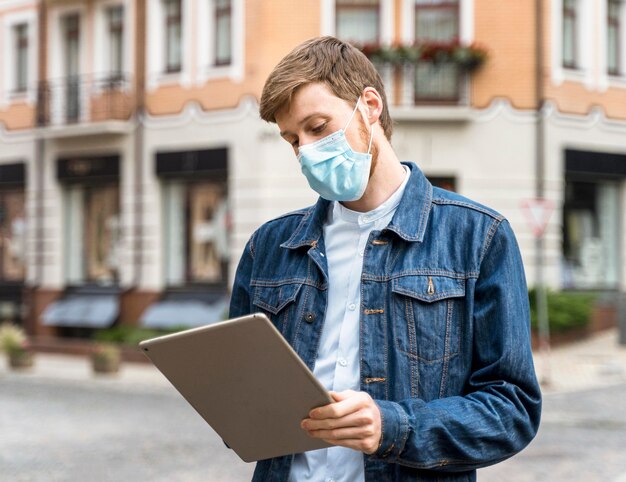 Foto uomo che tiene una compressa mentre indossa una maschera medica