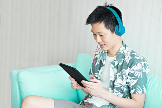 自宅のリビングルームで音楽を聴くためのヘッドフォン付きタブレットを保持している男。