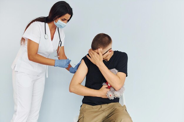 Man holding teddy bear during procedure Doctor in uniform making vaccination to the patient