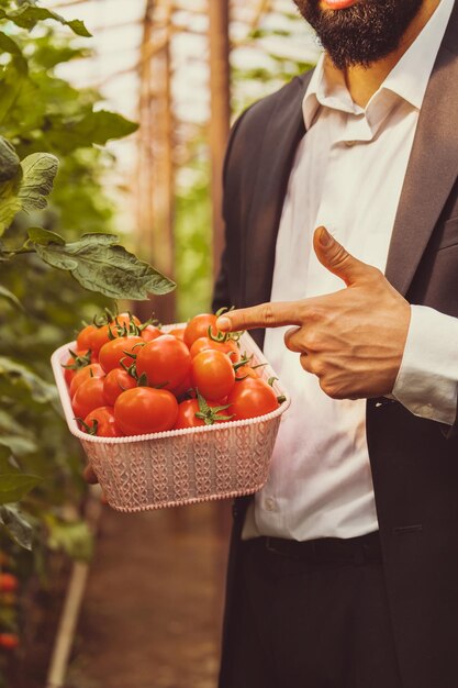 토마토 바구니를 들고 그것에 손가락을 가리키는 남자