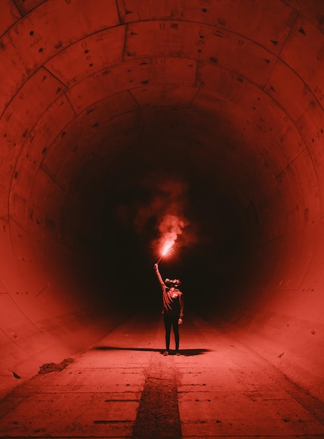 Foto un uomo con una torcia in un tunnel con uno sfondo rosso.