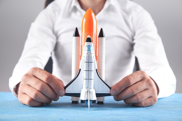 Photo man holding toy rocket on the desk.