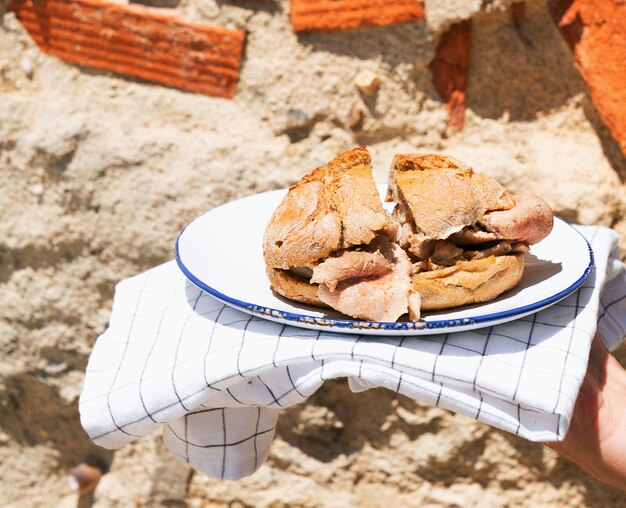 Man holding traditional portuguese Sandwich bifana over old brick wall. Street food concept