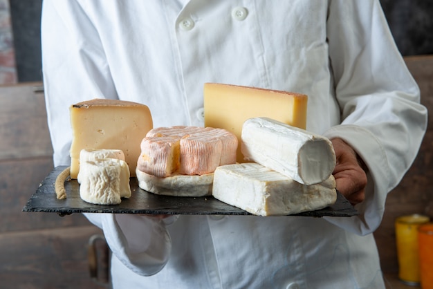 Мужчина держит поднос с различными французскими сырами