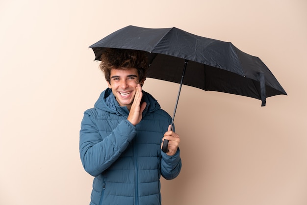 Man holding an umbrella over isolated wall whispering something