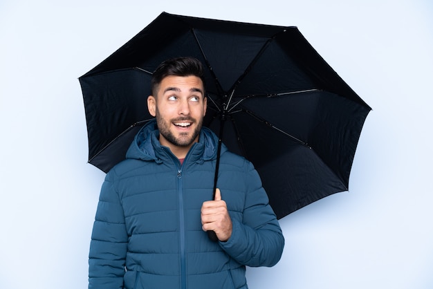 Мужчина держит зонтик над изолированной стеной с счастливым выражением