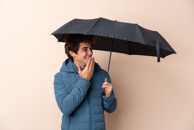 Man holding an umbrella over isolated wall with surprise and shocked facial expression