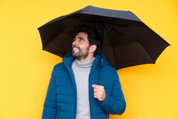 Man holding an umbrella over isolated yellow wall looking up while smiling