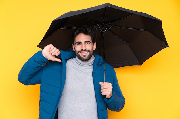 Мужчина держит зонтик над желтой стеной