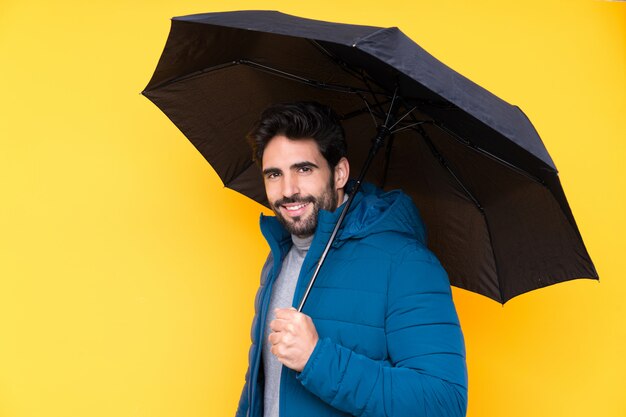 Man holding an umbrella over isolated yellow wall smiling a lot