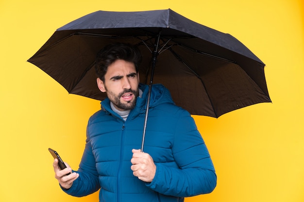 Мужчина держит зонтик над изолированной желтой стеной