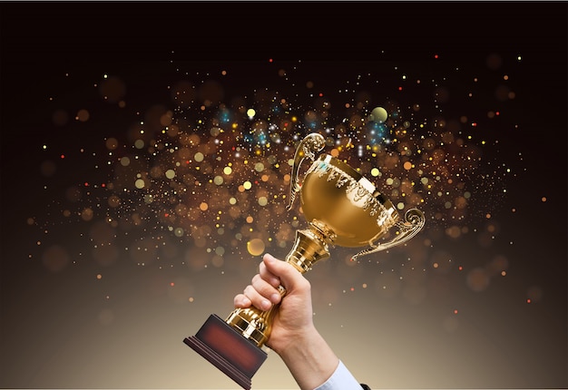 Man holding up a gold trophy cup with abstract shiny background, copy space for text