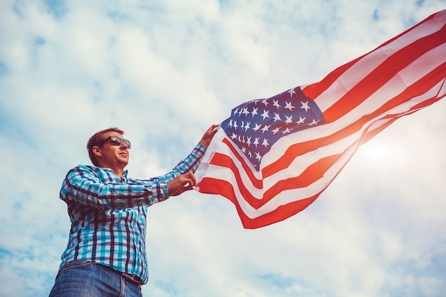 Мужчина держит флаг США против облачного неба