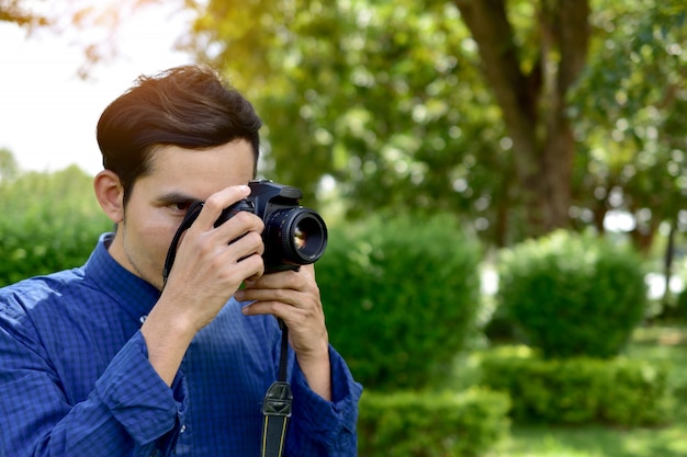 Equipaggi la tenuta e l'uso della macchina fotografica di dslr e la seduta sotto l'albero in parco pubblico sulla mattina