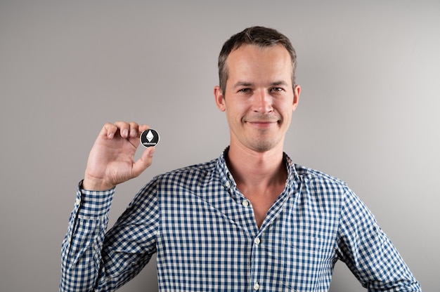 Man holding virtual currency ethereum coin and smiling. Crypto currency concept.