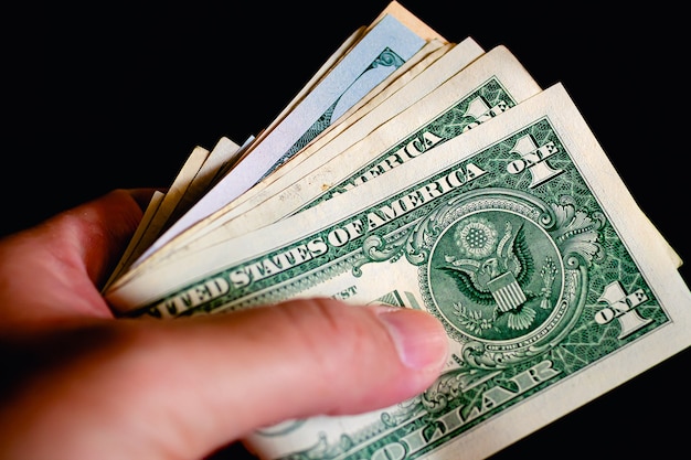 A man holding a wad of US dollar bills in closeup photo with black background