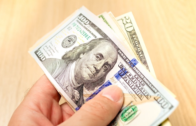 A man holding a wad of US dollar bills in closeup photo with wooden background