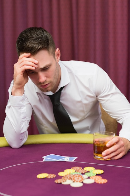 Uomo che tiene il bicchiere di whisky al tavolo da poker