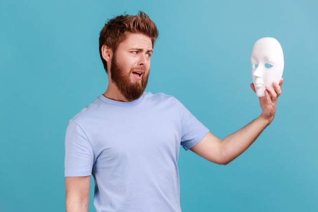 Man holding white mask in hands and looking with open mouth despises hidden personality