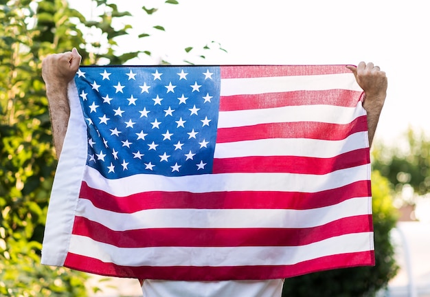 Un uomo che tiene con entrambe le mani la bandiera americana, per la giornata commemorativa del 4 luglio