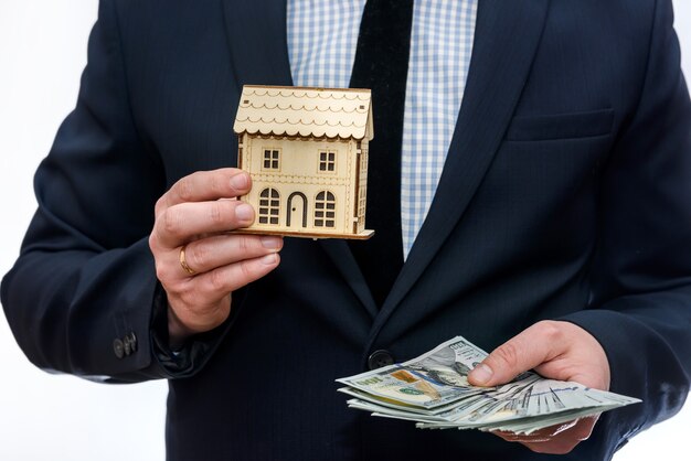 Man holding wooden house model and dollar banknotes