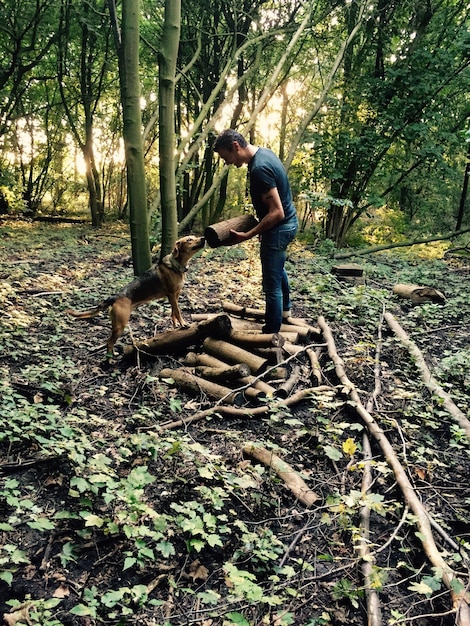 Foto uomo che tiene un tronco di legno con un cane in foresta.