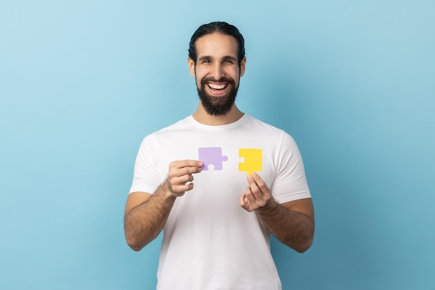 Man holding yellow and purple puzzle pieces solving tasks looking at camera with toothy smile