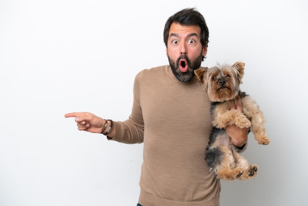 Man holding a yorkshire isolated on white background surprised and pointing side